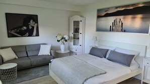 A bedroom with a bed, a sofa, a nightstand, a lamp, a vase with flowers, a cabinet, and a painting on the wall. - bunk by the water (Bezirk Spandau)