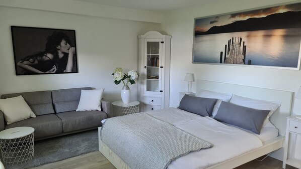 A bedroom with a bed, a sofa, a nightstand, a lamp, a vase with flowers, a cabinet, and a painting on the wall. - bunk by the water (Bezirk Spandau)