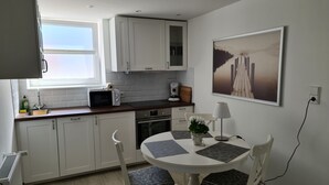 A modern kitchen with white cabinets, a microwave, a coffee maker, and a dining table with chairs. - bunk by the water (Bezirk Spandau)