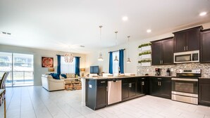 A modern kitchen with dark cabinetry, stainless steel appliances, and a central island. - Champions Gate Exec Villas- 9085hs (Davenport)