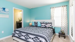 A bedroom with a large bed, a nightstand, a window with patterned curtains, and a door leading to another room. - Champions Gate Exec Villas- 9026sd (Davenport)