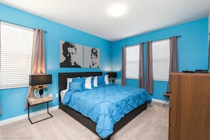 A bedroom with a blue wall, a bed with a blue bedspread, two bedside tables with lamps, and a wooden dresser.