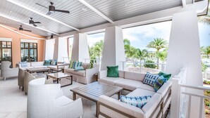 An outdoor lounge area with ceiling fans, comfortable seating, and large windows offering a view of palm trees and the beach. - Solara Resort Exec Villas- 1780spp (Kissimmee)
