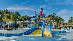 Parque acuático con una estructura de juego azul y amarilla, palmeras y un cielo azul despejado.