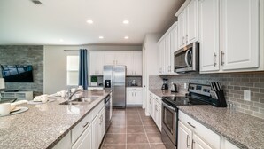Una cocina moderna con armarios blancos, encimeras de granito, electrodomésticos de acero inoxidable y un televisor de pantalla plana montado en la pared.