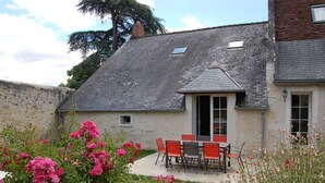 Une maison avec un patio, une table à manger avec des chaises et des fleurs en pleine floraison.