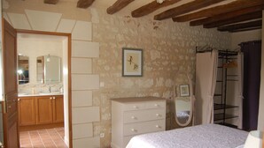 Une chambre à coucher avec un lit, une commode, un miroir et une salle de bain visible à travers une porte ouverte.