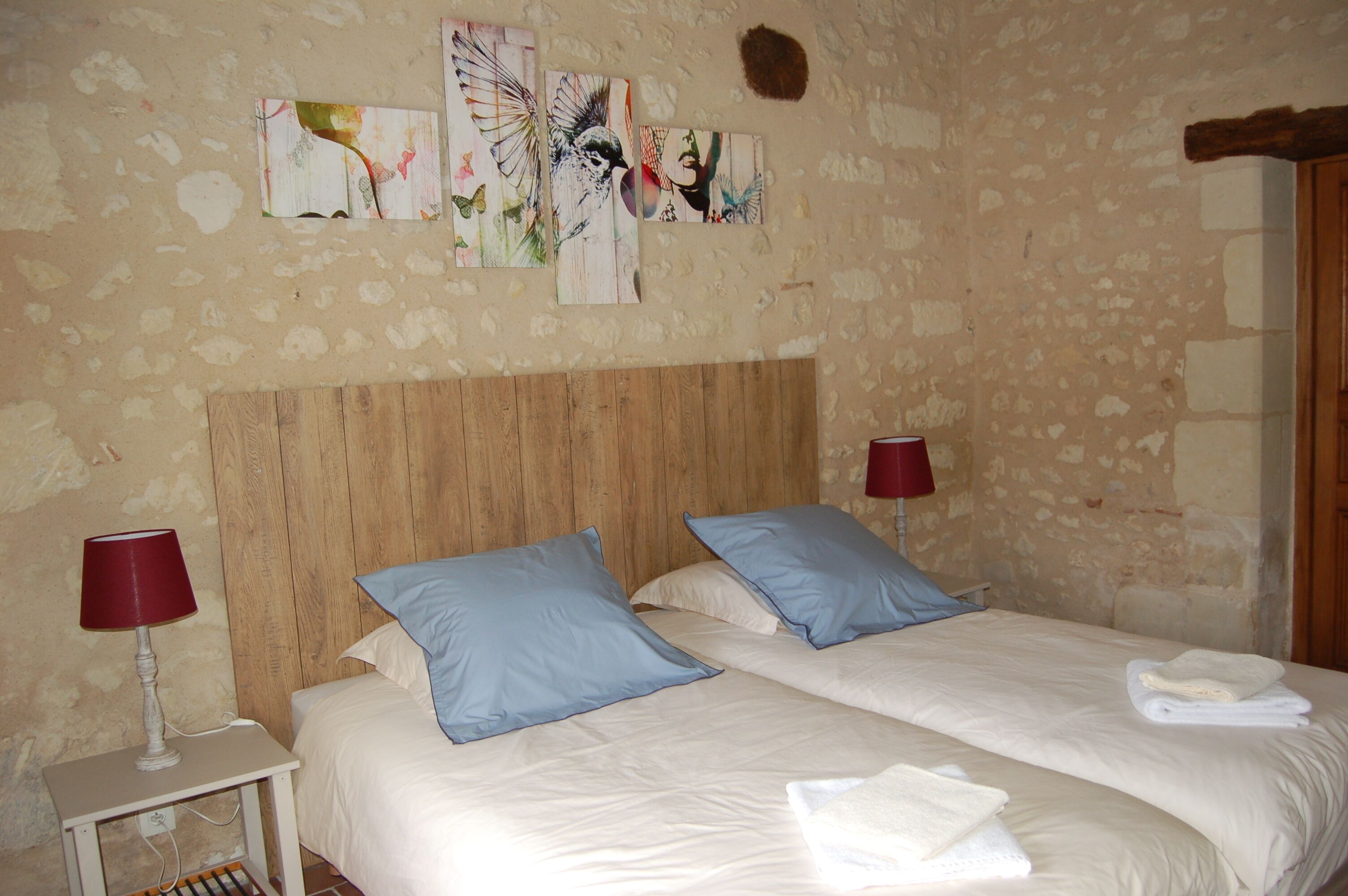 A bedroom with two beds, wooden headboard, red lamps, and artwork on the wall.