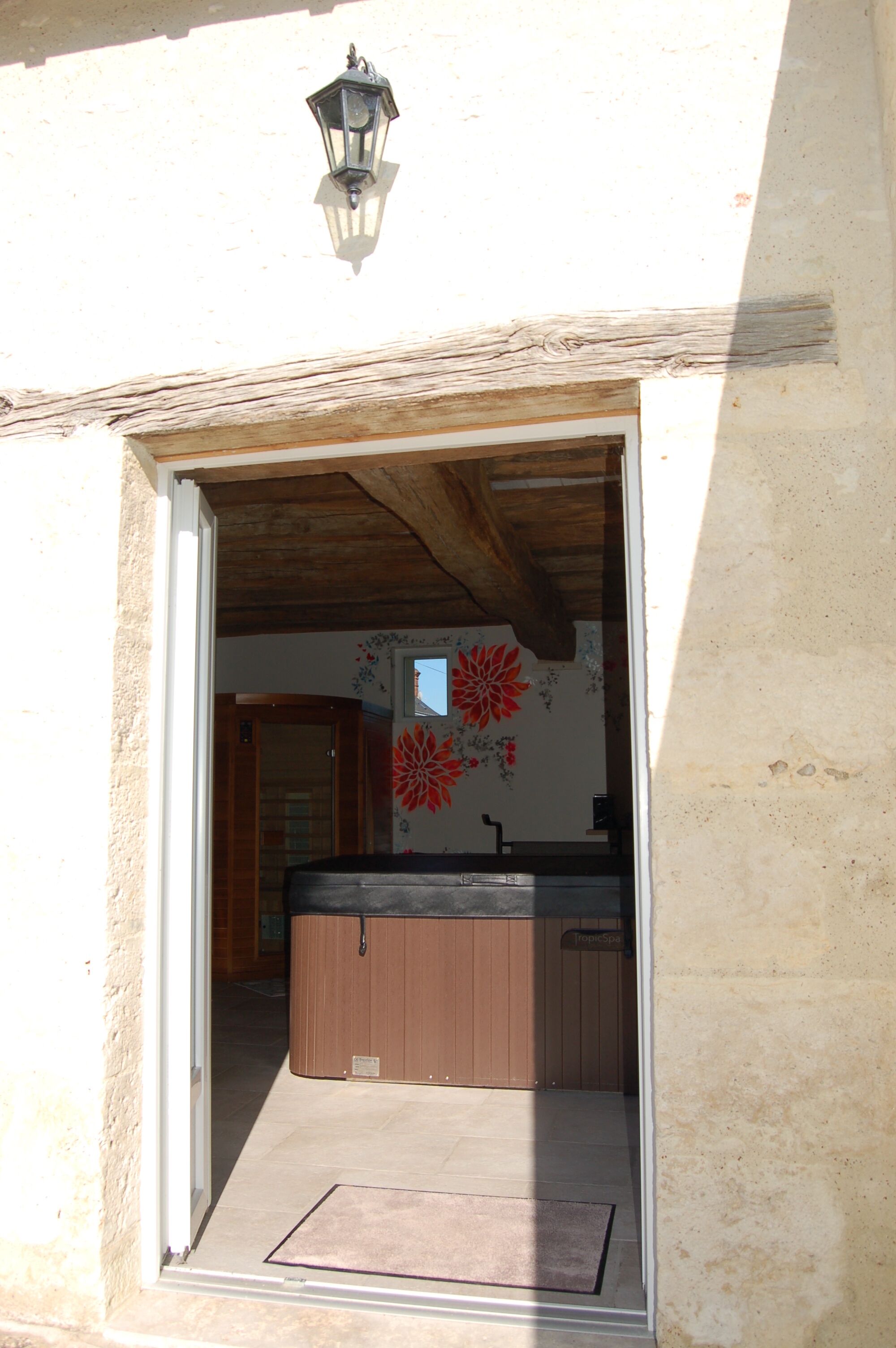 Una puerta de madera que da a un cuarto con un ventanal grande y un adorno floral rojo en la pared.