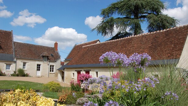 Un bâtiment de style européen traditionnel, avec un toit en briques et un jardin où poussent différentes sortes de fleurs.
