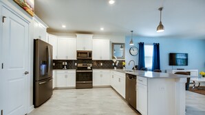 A modern kitchen with white cabinets, stainless steel appliances, a central island, and a blue accent wall. - Champions Gate Exec Villas- 1584sandb (Davenport)