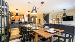 Et moderne køkken med træskabe, et spisebord dækket til seks personer og en trappe til en etage ovenover.