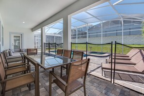Eine überdachte Terrasse mit einem Glastisch und Stühlen, einem Pool und Liegestühlen.