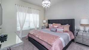 Een slaapkamer met een groot bed, nachtkastjes, een glazen bureau en een kroonluchter.