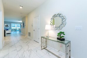 A hallway with a glass console table, a decorative mirror, and a potted plant. - Champions Gate Exec Villas- 1586sandb (Davenport)