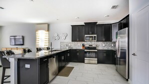 Una cucina moderna con mobili scuri, elettrodomestici in acciaio inossidabile e una parete a mosaico in marmo.