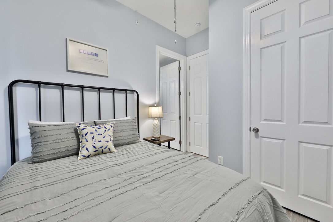 A bedroom with a bed, a nightstand, a lamp, and a door.
