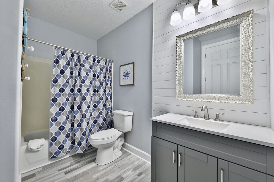 A bathroom with a patterned shower curtain, a toilet, a sink with a mirror, and a cabinet.