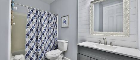 A bathroom with a patterned shower curtain, a toilet, a sink with a mirror, and a cabinet.