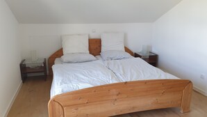 Une chambre à coucher avec un lit en bois, du linge de lit blanc et une table de chevet avec une lampe.