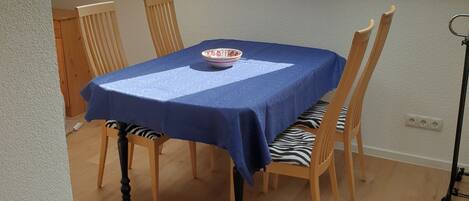 Un comedor con una mesa cubierta con mantel azul, sillas de madera y un tazón sobre la mesa.