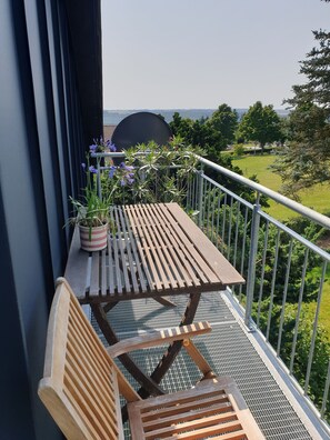 A balcony with a wooden table and bench, potted plants, and a view of a park.