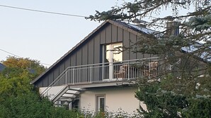 Une maison à deux étages dotée d’un balcon, entourée d’une végétation luxuriante.