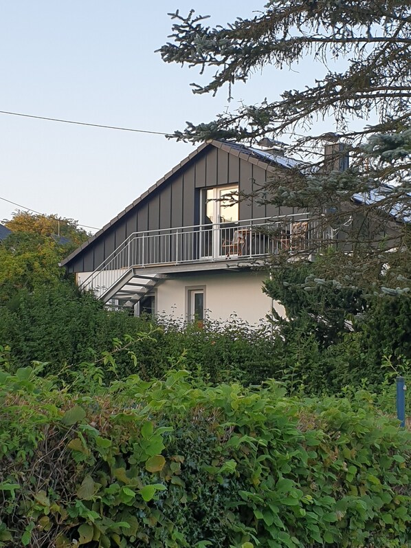 A two-story house with a balcony, surrounded by dense greenery.