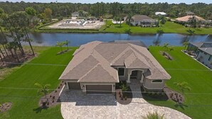 A single-story house with a large driveway, a covered patio, and a view of a lake.