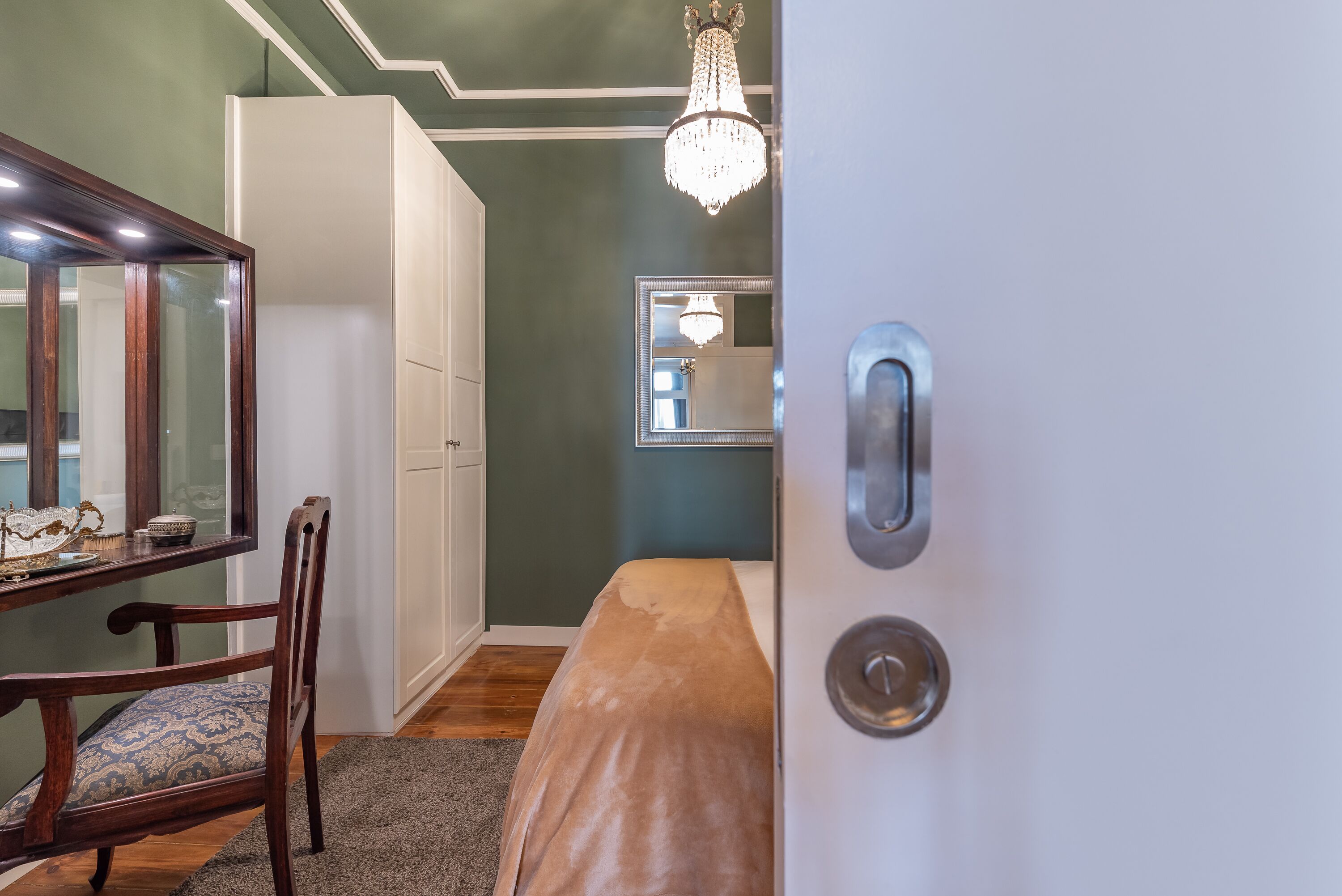 A room with a wooden chair, a bench, a mirror, and a chandelier.