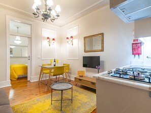 A modern living room with a dining area, a kitchen with a gas stove, a chandelier, and a large mirror on the wall.