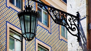 A traditional street lamp with a decorative design, attached to a building with a patterned facade. - Portuguese Charm in Lisbon (Lisboa)