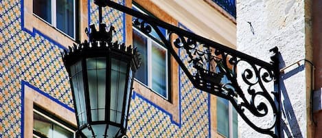 Una farola tradicional con diseño decorativo, adosada a un edificio con fachada ornamentada.