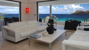 A modern living room with a white sofa, a coffee table, and a view of the ocean and a distant island.