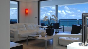 A modern living room with a white sofa, a coffee table, and a potted plant. There is a large window with a view of the ocean.