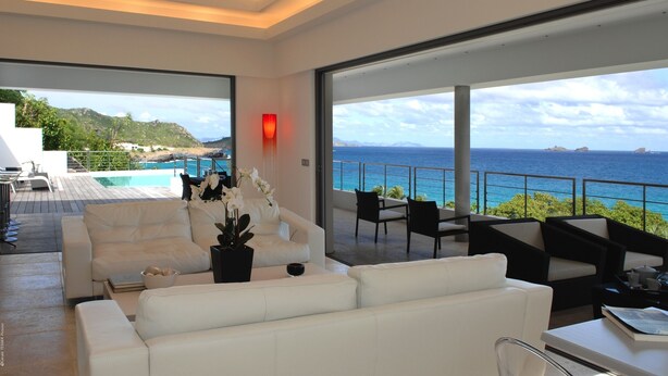 A modern living room with a white sofa, black chairs, and a view of the ocean.