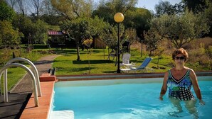 En swimmingpool med en terrass av tegelsten, ett parasoll och en solstol.