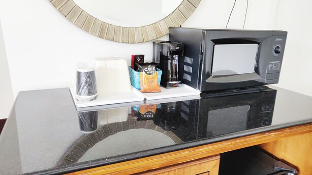 A kitchen counter with a coffee maker, a cup, and a bag of coffee. - Countryside Inn (Richmondville)
