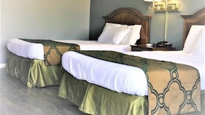 A hotel room with two beds, each with a green bed skirt and white linens. There is a nightstand with a lamp between the beds. - Countryside Inn (Richmondville)