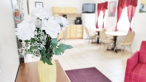A room with a wooden table, a yellow vase with white flowers, a red couch, and a dining area with chairs and a table. - Countryside Inn (Richmondville)