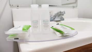 A bathroom sink with three bottles of shampoo and two packets of conditioner.