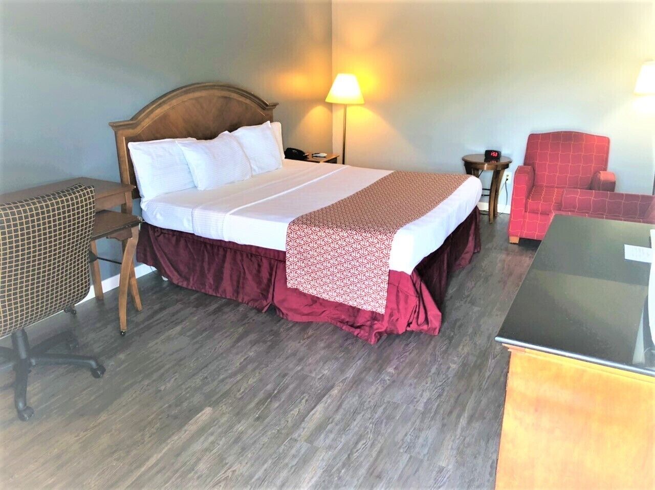 Una habitación de hotel con cama, mesita de noche, lámpara, silla y escritorio.