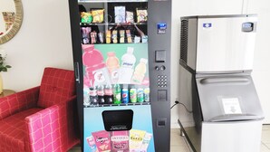 A vending machine stocked with snacks and drinks, a red chair, and a refrigerator. - Countryside Inn (Richmondville)