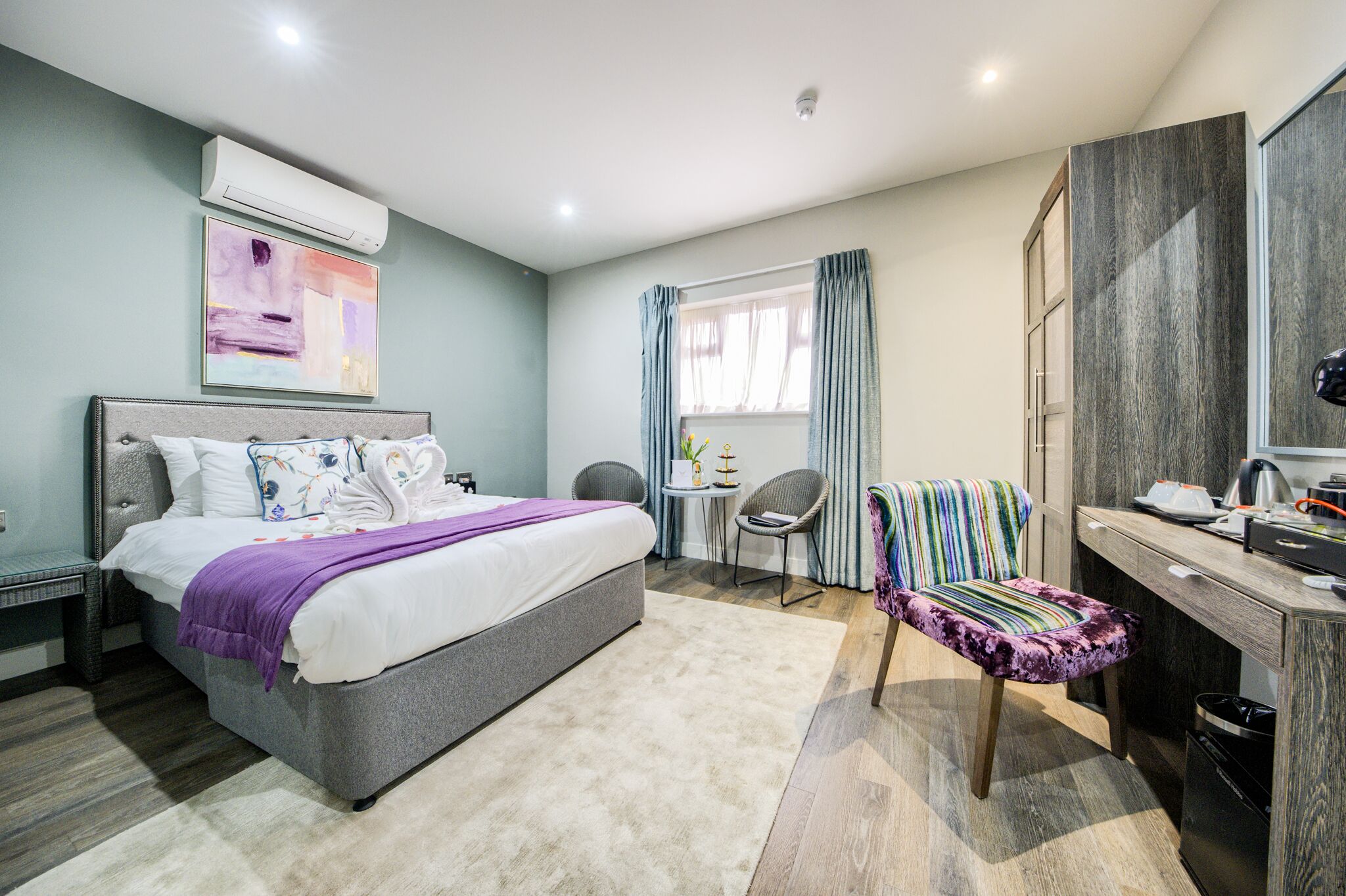 Een moderne hotelkamer met een groot bed, een bureau, een stoel en een bijzettafeltje met een plant.