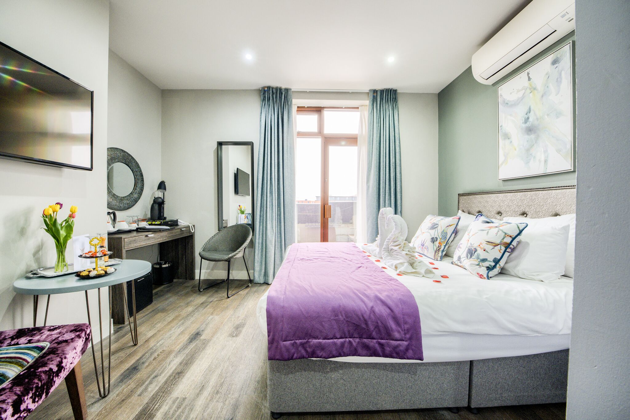 A modern hotel room with a bed, desk, chair, and a small table with flowers.