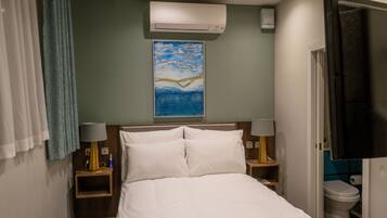 Hotelkamer met een bed, twee bedlampen, een airconditioner, een schilderij aan de muur, een badkamer met toilet en een aan de muur bevestigde televisie.