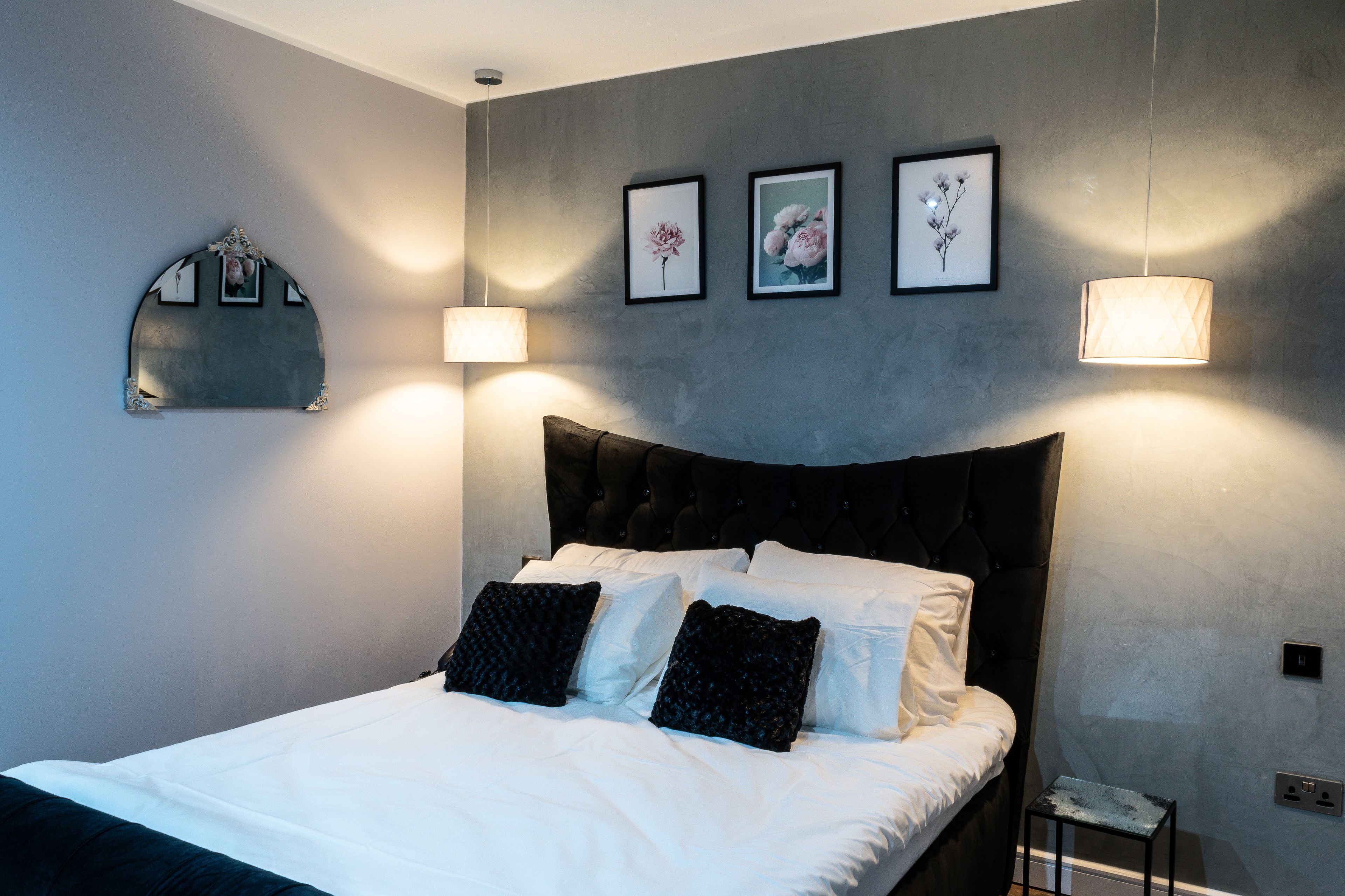 Um quarto com cama, mesa de cabeceira e luminárias fixadas na parede.