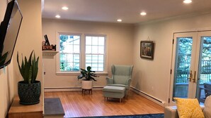 A spacious living room with hardwood flooring, a blue patterned rug, a light blue armchair, a white sofa with a yellow pillow, and a glass coffee table. - A dream summer rental 30 miles from New York City in picturesque Bedford, NY! (Bedford)