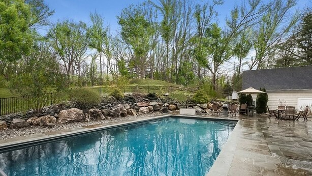 A rectangular swimming pool with a stone border, surrounded by a stone wall and a metal fence. - A dream summer rental 30 miles from New York City in picturesque Bedford, NY! (Bedford)