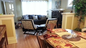 A dining area with a wooden table set for four, surrounded by chairs. A sofa is visible in the background, and a plant is on the right side. - Butte Bungalow Home, Close to uptown- 2 bdrm, 2 bath, No Cleaning fee (Butte)